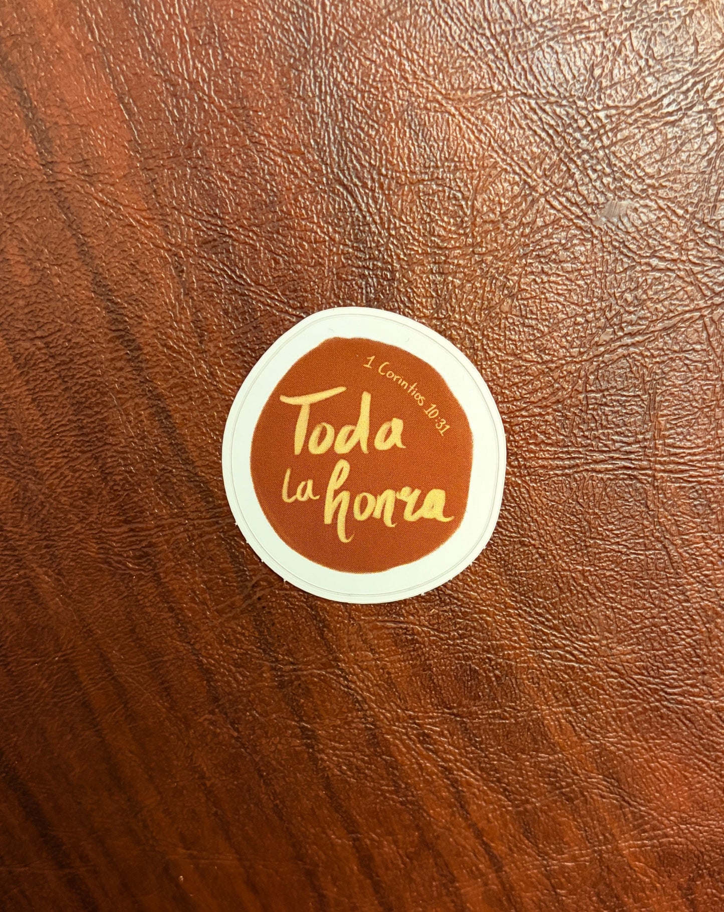 Round sticker with 'Toda la honra' text on a brown leather surface
