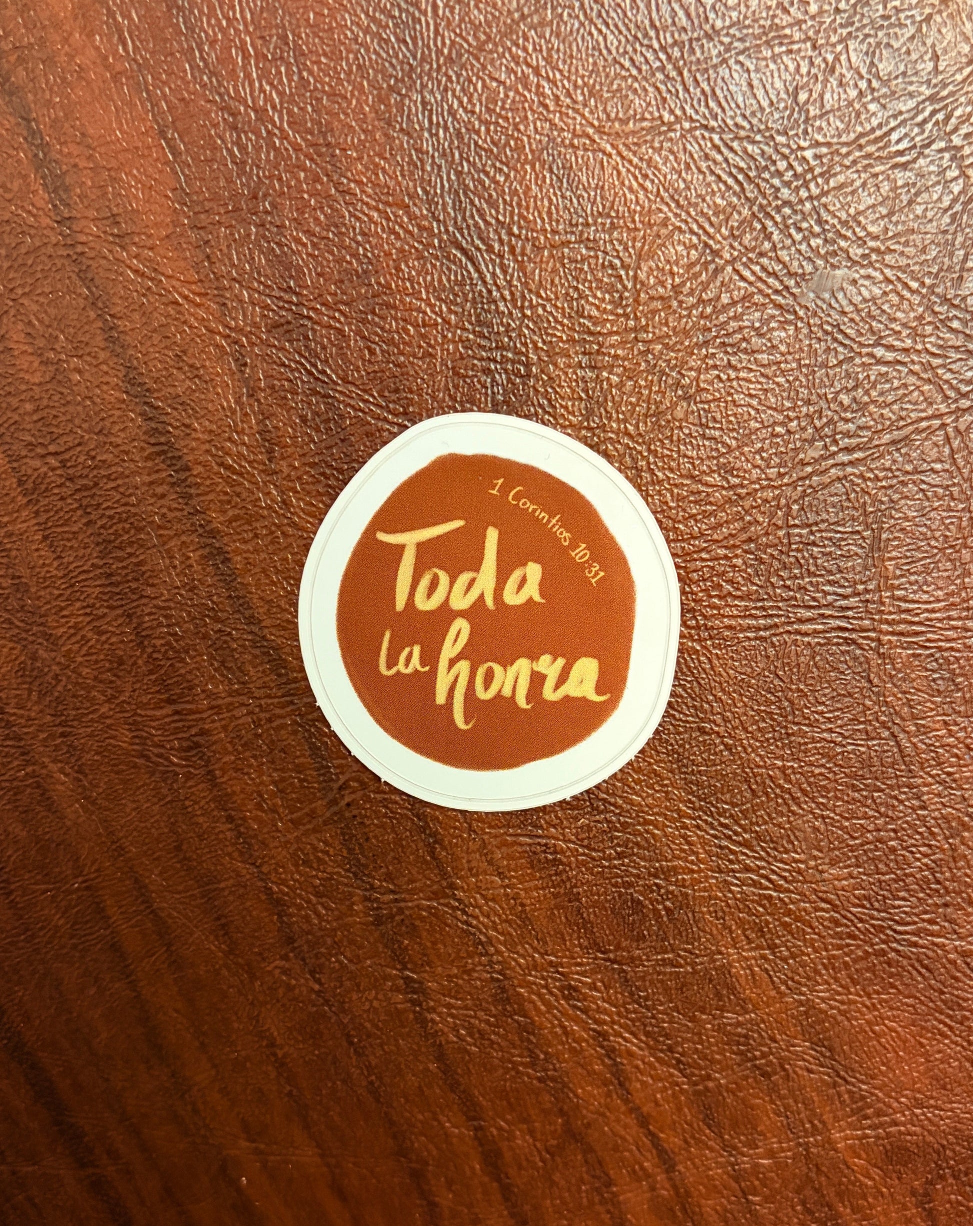 Round sticker with 'Toda la honra' text on a brown leather surface