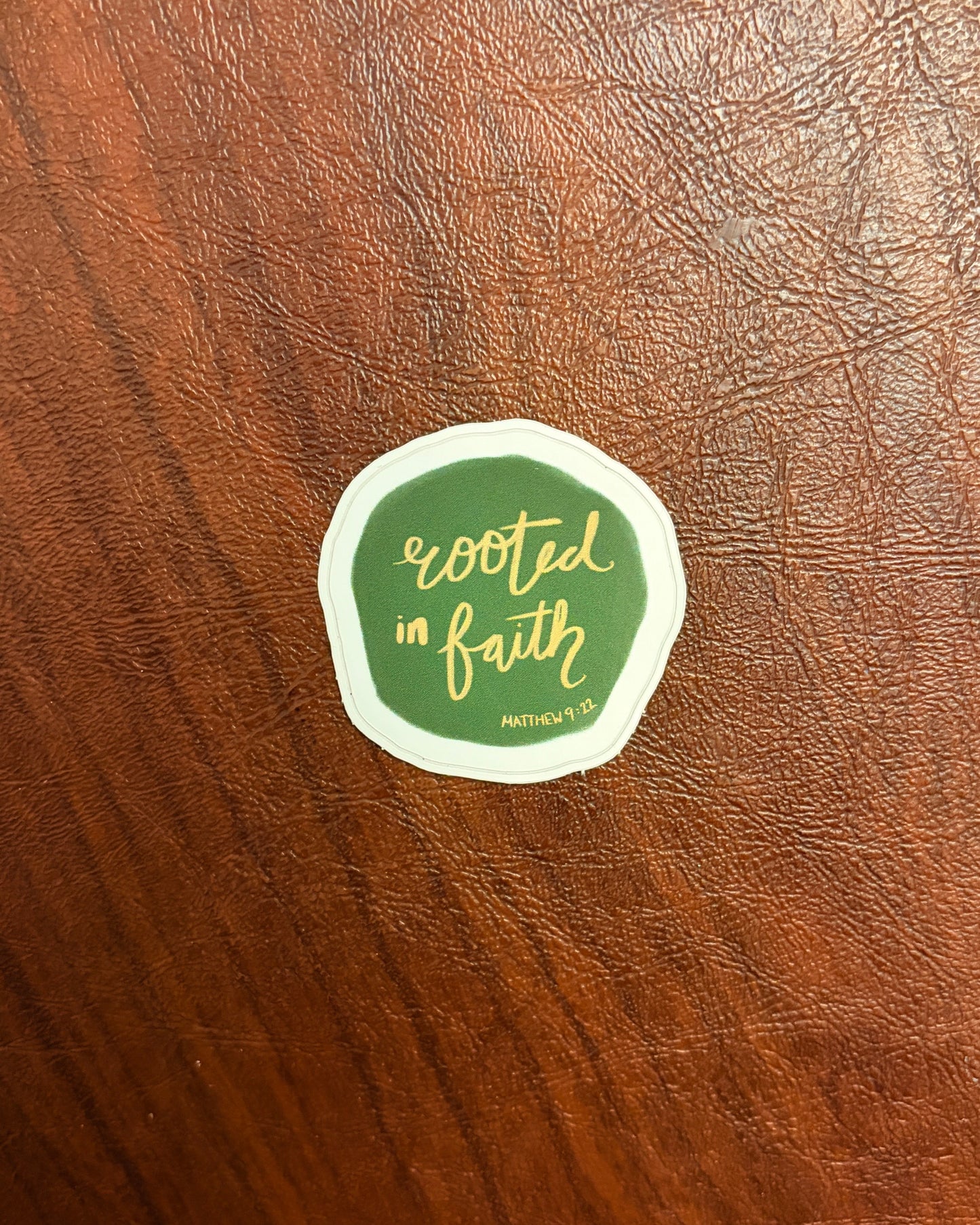 Green sticker with 'Rooted in Faith' text on a wooden surface