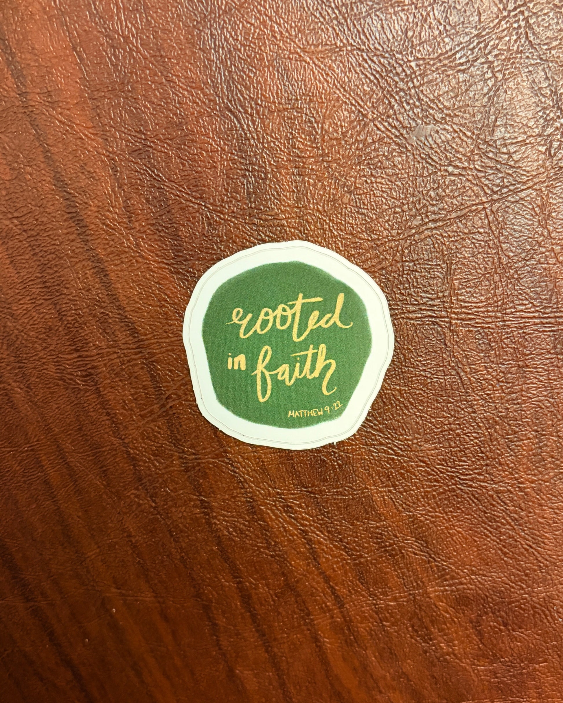 Green sticker with 'Rooted in Faith' text on a wooden surface